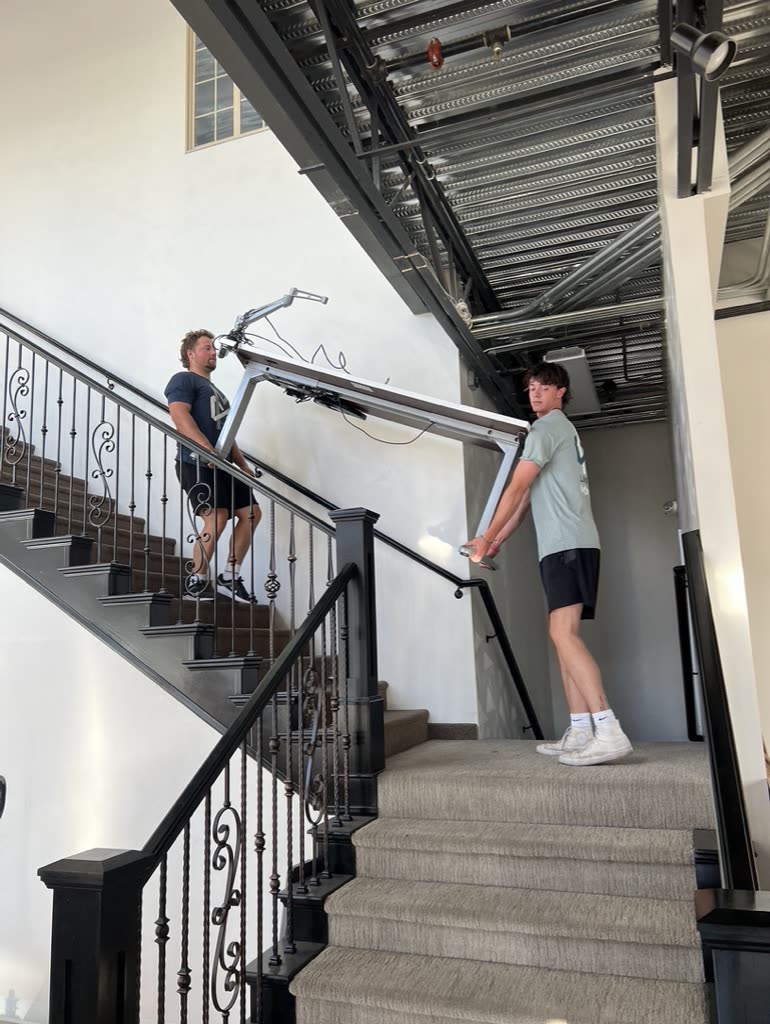 Two Limitless movers carrying a large piece down a staircase